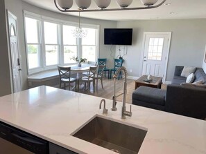 A modern kitchen with a large island, a dining area with chairs, a sofa, and a flat-screen TV mounted on the wall. - Premier Oceanfront Beach Pad 9BR (Atlantic City)