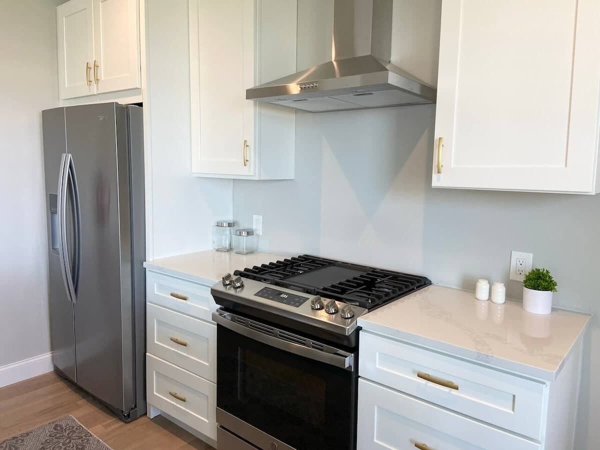 Una cocina con armarios blancos, un refrigerador de acero inoxidable, una estufa a gas y una campana extractora.