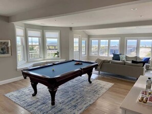 A pool table in a room with large windows, a sofa, and a view of the outdoors. - Premier Oceanfront Beach Pad 9BR (Atlantic City)
