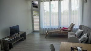 Una sala de estar con un televisor sobre un mueble de madera, un sofá con cojines estampados, una mesa de centro de madera y un sillón con un cojín rojo.