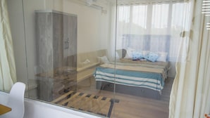 Un dormitorio con cama, mesita de noche, armario y ventana con cortinas.