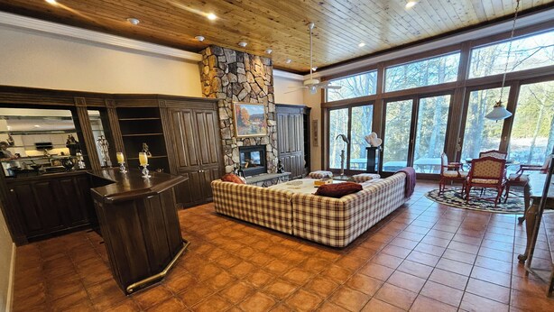 Amplia sala de estar con chimenea, un gran ventanal que ofrece vistas al exterior y una cocina con muebles de madera oscura.