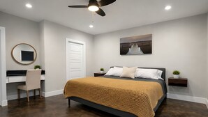 Un dormitorio con cama, escritorio, silla, ventilador de techo y televisión instalada en la pared.