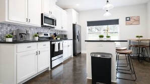 Una cocina moderna con armarios blancos, electrodomésticos de acero inoxidable, una isla negra y una zona de comedor con taburetes.