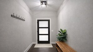 Un pasillo con un banco de madera, una puerta con paneles de vidrio esmerilado, un perchero en la pared y una planta en maceta.