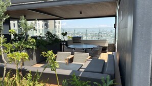 Una terraza en la azotea con mobiliario exterior, una mesa redonda y vistas de la ciudad.