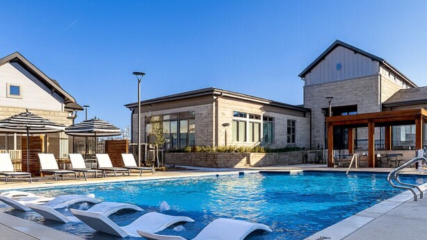 En swimmingpool med liggestole og en bygning med store vinduer.