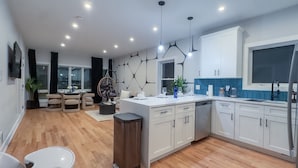 A modern kitchen with white cabinets, a dining area with a hanging chair, and a large window. - Pristine Pad, Sleep 9, Free driveway park, 20%OFF (East Newark)