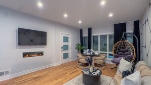 Ein modernes Wohnzimmer mit Flachbildfernseher, Kamin, Essbereich und Hängesessel.