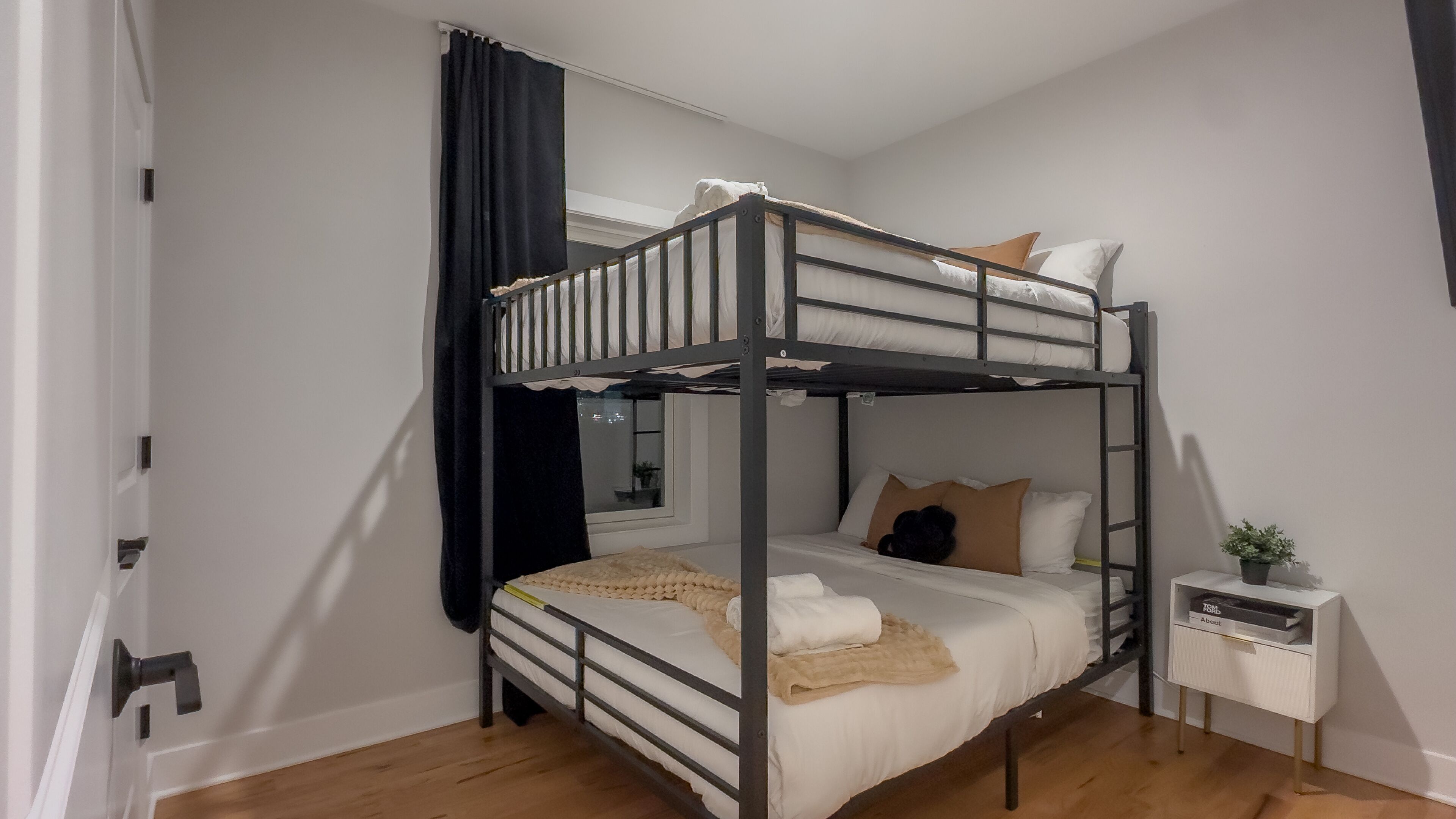 A bunk bed room with a window, a bedside table, and a small plant.