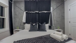 Ein modernes Schlafzimmer mit einem großen Bett, schwarz-weißen Vorhängen und einem grauen Teppich mit Struktur.