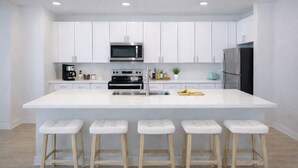 Une cuisine moderne avec des meubles blancs, un îlot central doté de tabourets, un four à micro-ondes, une cuisinière et un réfrigérateur.