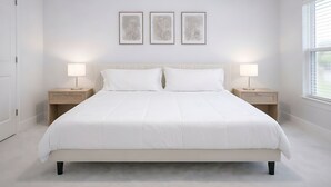 Une chambre à coucher moderne avec un grand lit, deux tables de chevet avec des lampes et trois œuvres d’art encadrées accrochées au mur.
