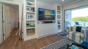 A living room with a built-in entertainment unit, a large painting, and a view through a glass door. - Dolphin Paradise- Peaceful 1-bedroom condo in historic Old Marco Island (Marco Island)