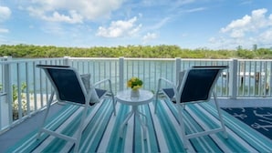 A balcony with two chairs and a small table, overlooking a body of water and a forested area. - Dolphin Paradise- Peaceful 1-bedroom condo in historic Old Marco Island (Marco Island)