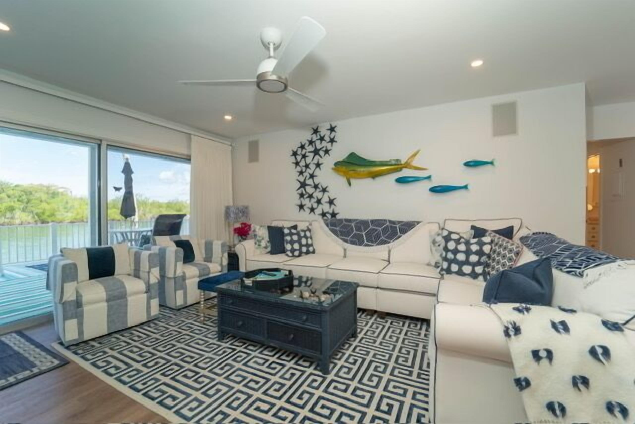 A modern living room with a white sofa, striped armchairs, a coffee table, and decorative fish wall art.