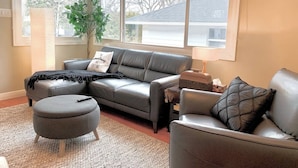 A living room with a sectional sofa, a round ottoman, and a small side table. - VIP YXE - Broadway |Three Bedroom Main Floor Suite (Saskatoon)