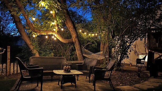 An outdoor patio area with wicker furniture, a round table, and string lights. - VIP YXE - Broadway |Three Bedroom Main Floor Suite (Saskatoon)