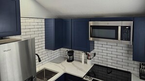 Una cocina moderna con baldosas blancas tipo metro, armarios azul oscuro, un refrigerador de acero inoxidable, un microondas y una cafetera.