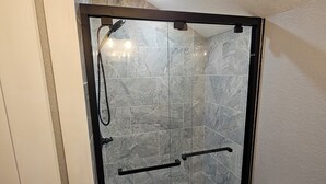 Un baño con ducha envuelta en vidrio, inodoro y baldosas de mármol.