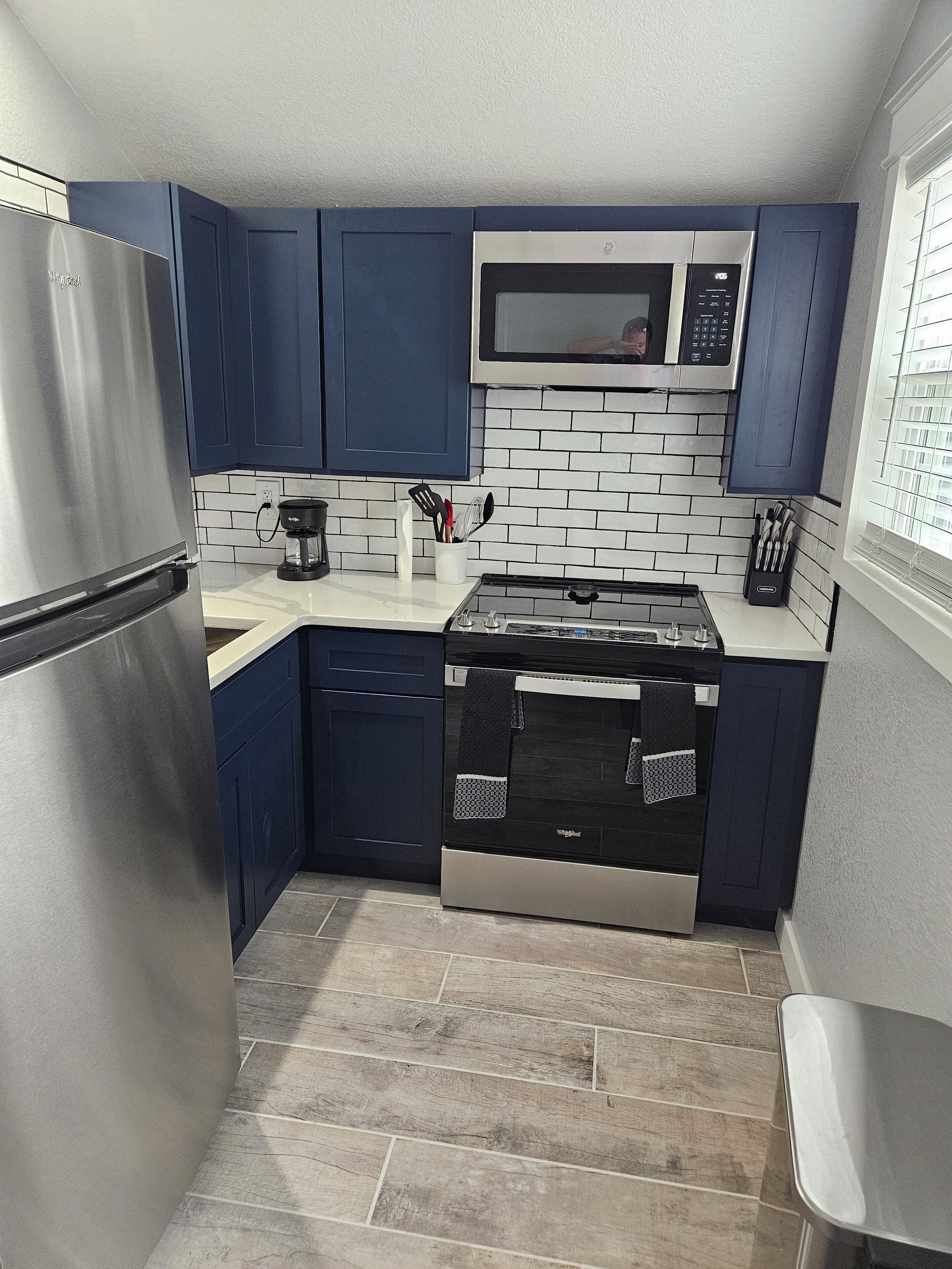 Cocina compacta con armarios azul oscuro, un refrigerador de acero inoxidable, un microondas y una estufa a gas.