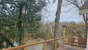 Una terraza de madera con barandilla que da a un río, rodeada de árboles.