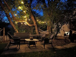 Un espacio al aire libre con patio, muebles de mimbre, una mesa redonda y luces colgantes.