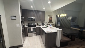 A modern kitchen with stainless steel appliances, a marble countertop, and a dining area with a wooden table and bench. - Park City, Ski-in, Ski-out, 2-bed 2 bath, Sleeps 8 (Park City)