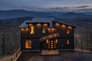 Ein modernes, zweistöckiges Haus mit Metallverkleidung, großen Fenstern und einem gut beleuchteten Eingangsbereich.