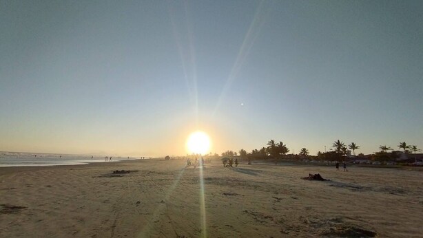 A beach with the sun setting in the distance, palm trees, and a few people walking. - Simple house near Praia Sonho - Itanhaém (family/small groups) (Itanhaém)
