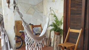 A hammock on a tiled patio with a wooden chair, a bicycle, and a potted plant. - Simple house near Praia Sonho - Itanhaém (family/small groups) (Itanhaém)