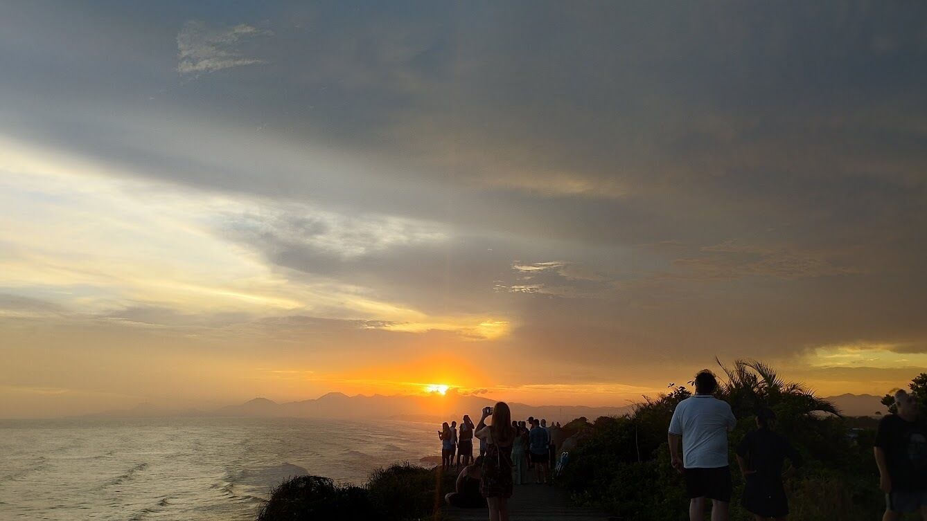 Une vue sur le coucher de soleil depuis une zone côtière, où l’on peut voir des personnes qui observent le soleil.