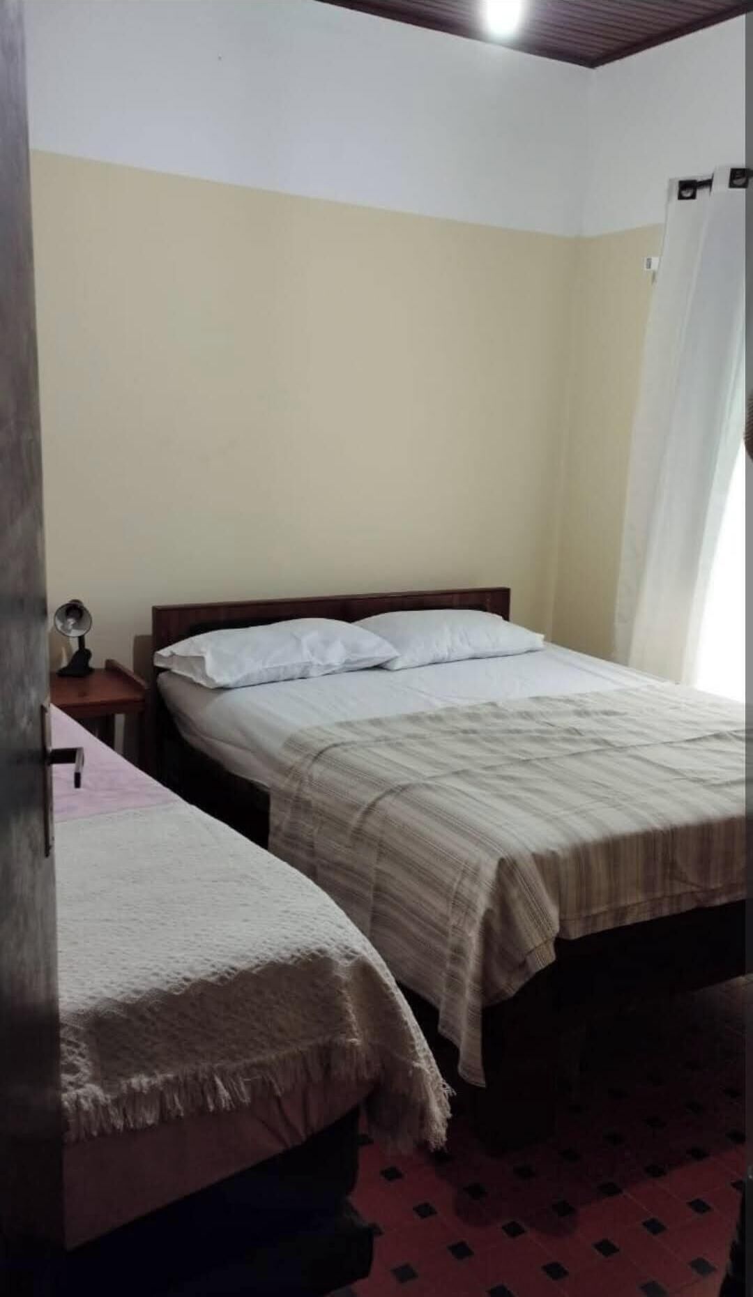 A bedroom with two single beds, a nightstand with a lamp, and a window with curtains.