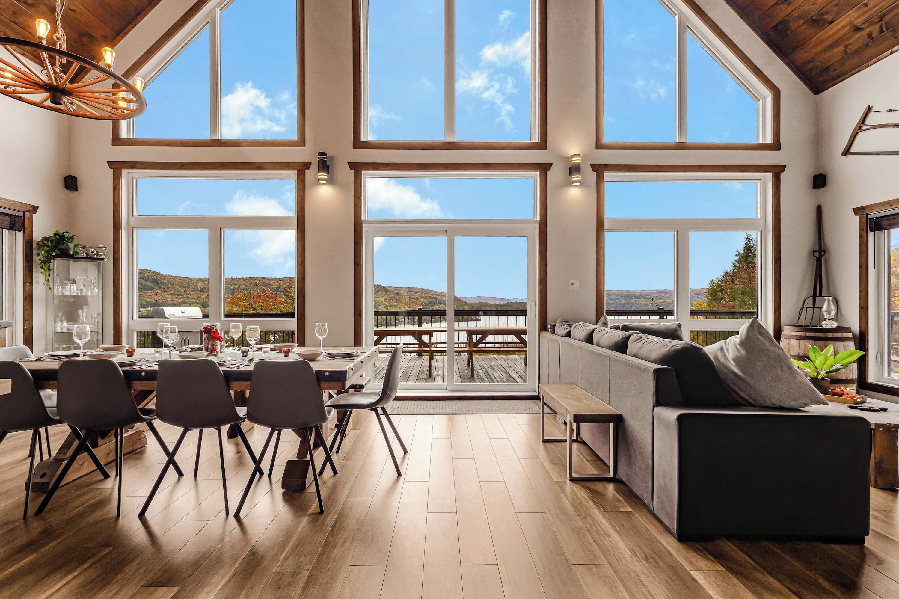 A spacious dining area with a wooden table and chairs, a large window with a view of the landscape, and a cozy seating area with a sofa and cushions.