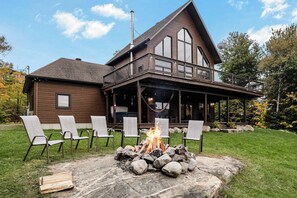 A two-story house with a large balcony, a fire pit, and outdoor seating.