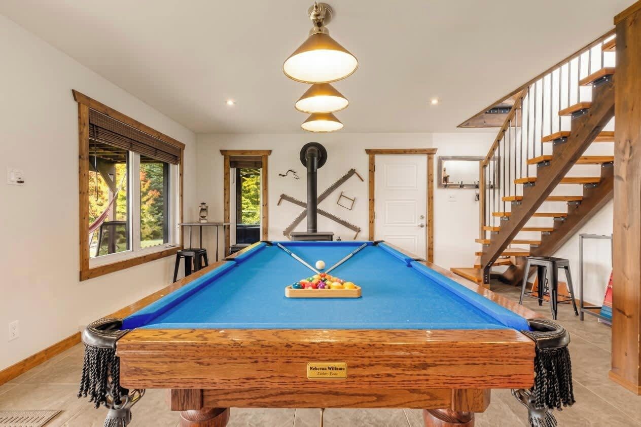Una mesa de billar con una placa, una escalera y un ventanal con vistas a árboles.