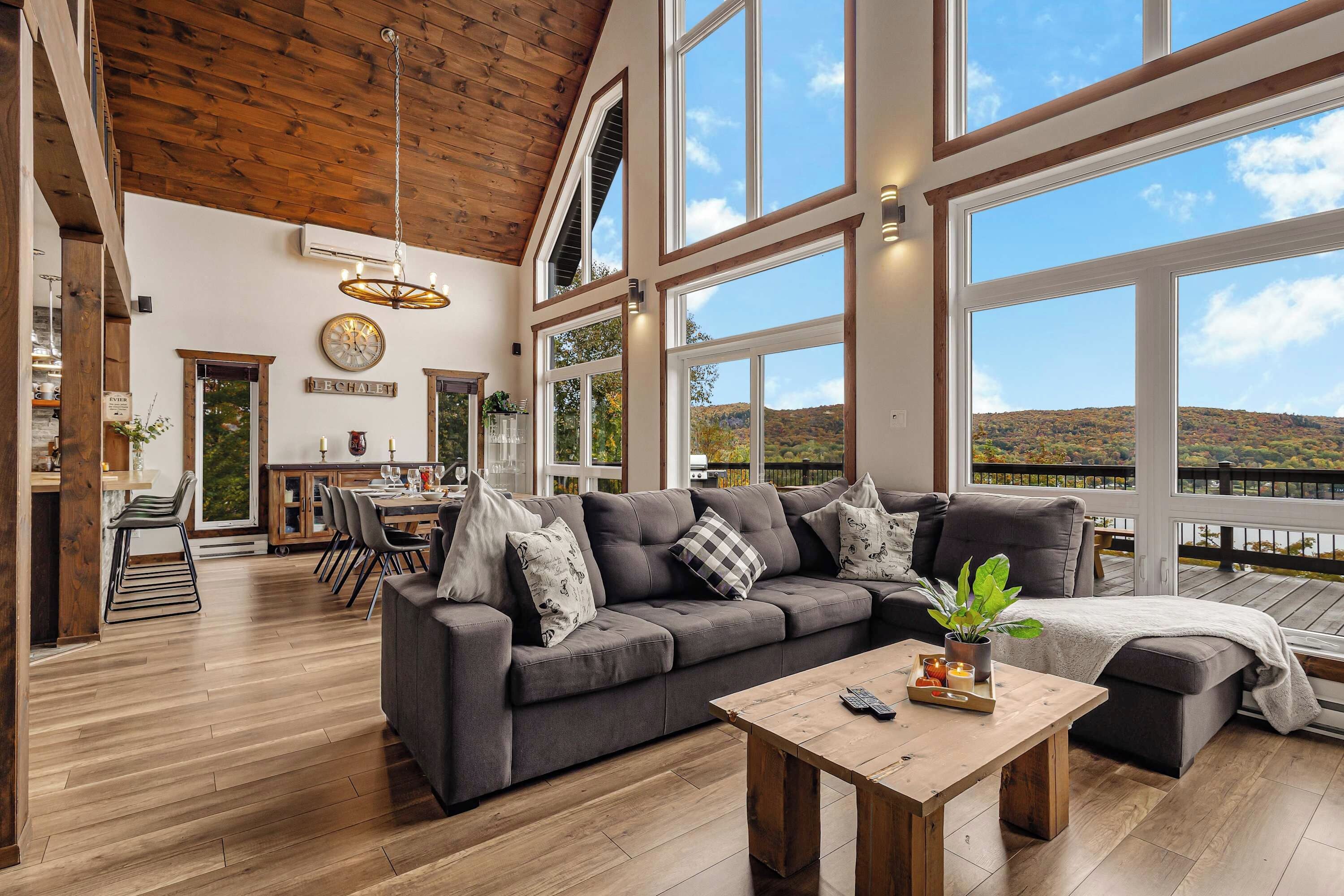 A spacious living area with a large gray sofa, wooden coffee table, and a view of the outdoors through large windows.