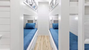 Une pièce étroite aux murs blancs, comprenant deux lits, chacun recouvert d’une couverture bleue et doté d’une tête de lit, et un plancher en bois.