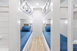 Ein schmales Zimmer mit weißen Wänden, zwei Betten mit blauen Bettdecken und Kopfteilen sowie einem Holzboden.
