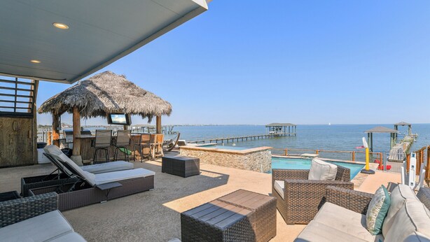 A sunlit outdoor lounge area with wicker furniture, a pool, and a view of the sea and pier. - Private Pier & Pool / 5 min to Kemah Boardwalk (Kemah)