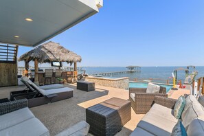 A sunlit outdoor lounge area with wicker furniture, a pool, and a view of the sea and pier. - Private Pier & Pool / 5 min to Kemah Boardwalk (Kemah)