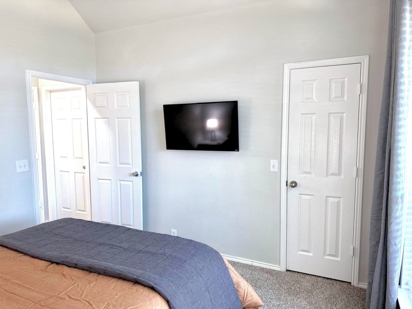 A bedroom with a bed, a television mounted on the wall, and two white doors.