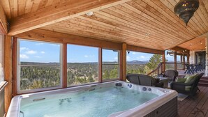 A hot tub on a wooden deck with a view of a forest and mountains.