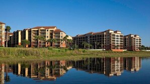 Un hotel con varias construcciones, un reflejo en el agua y palmeras.