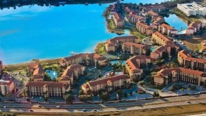 Vista aérea de un resort con varias construcciones, una gran masa de agua y una autopista en primer plano.