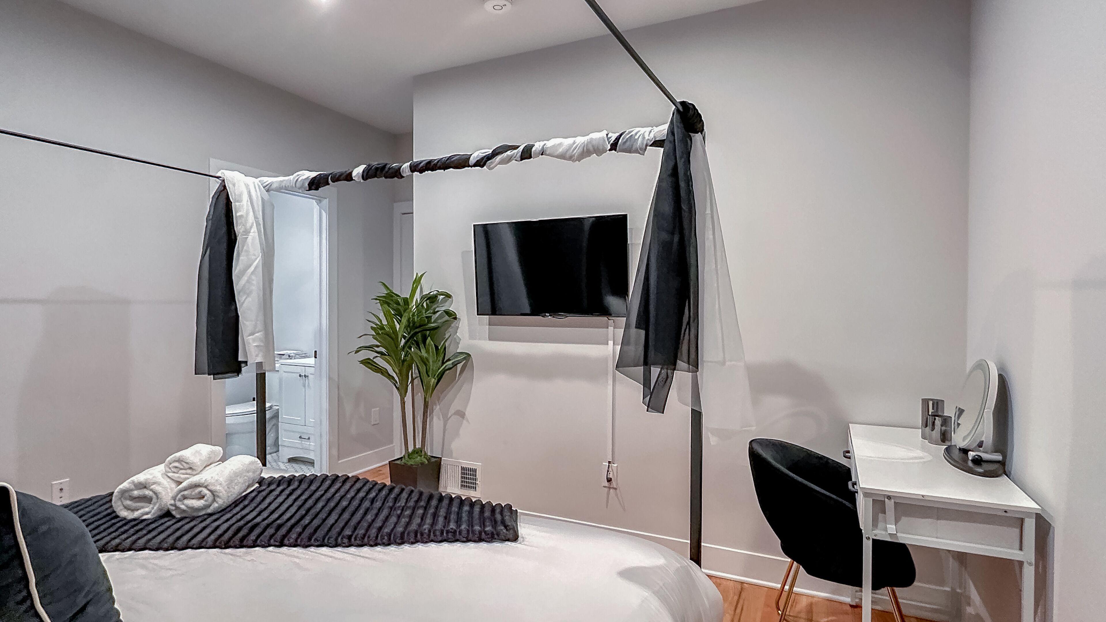 A modern bedroom with a bed, a desk, a chair, a TV, and a plant.
