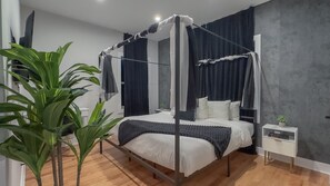 Un dormitorio moderno con cama con dosel, mesita de noche, planta en maceta y otro mesita.