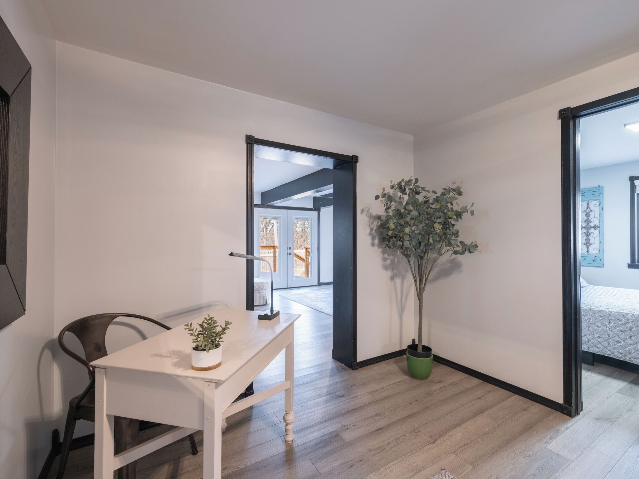 Et moderne, minimalistisk værelse med trægulv, et hvidt skrivebord med en plante og et stort vindue.