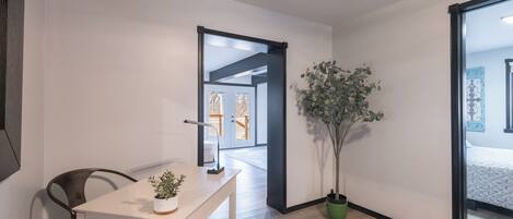 Et moderne, minimalistisk værelse med trægulv, et hvidt skrivebord med en plante og et stort vindue.