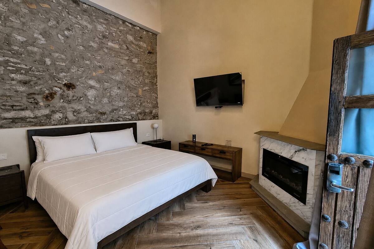 Ein Schlafzimmer mit Steinwand, einem Bett, einem Fernseher, einem Kamin und Holzboden.